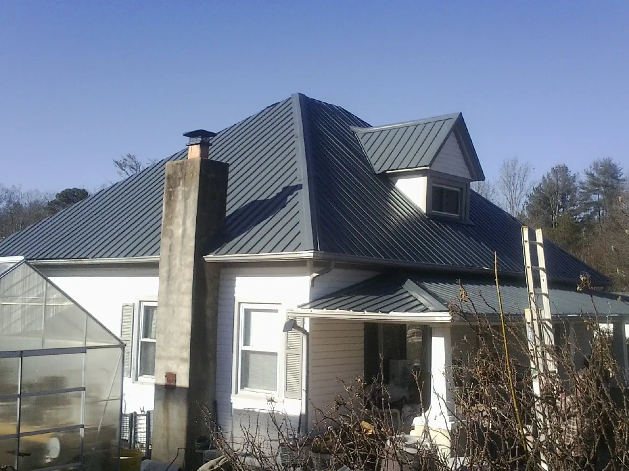 Dark blue standing seam metal roof on a white farmhouse with dormer — Slate & Tile Roof Repair by Roofing Brothers in Oakton
