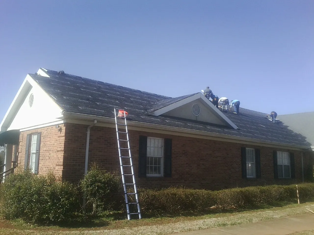 Crew tearing shingles off a brick ranch roof with a ladder set — Emergency Roof Repair work by our crew in Oakton