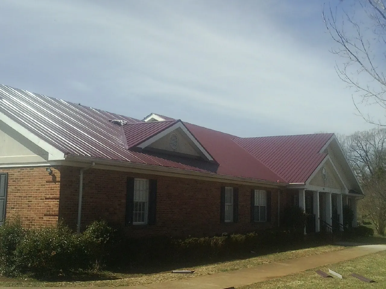 Red metal roof with gabled entries on a long brick building, from a Hail Damage Roof Repair job in Oakton