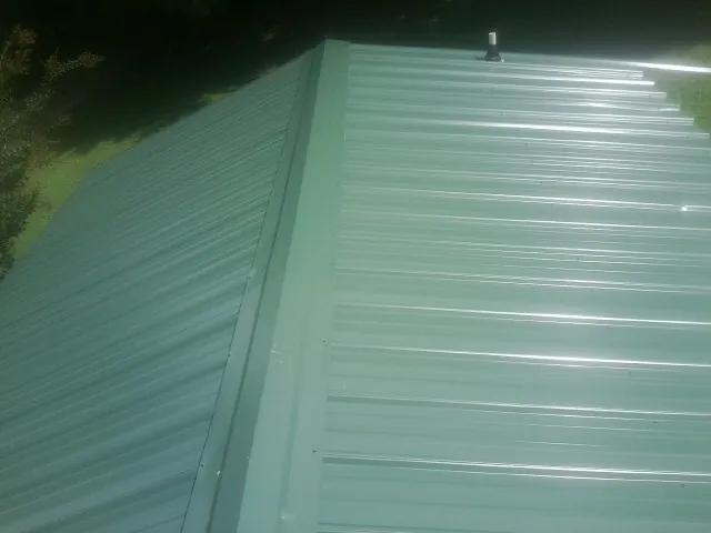 New green metal panels meeting at the ridge of a roof — Flat Roof Repair work by our crew in Oakton