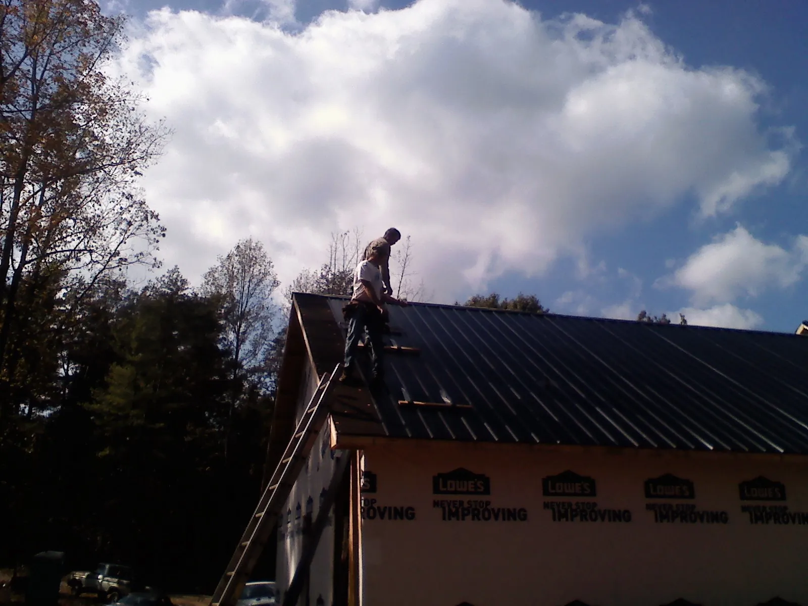 Roofer fastening dark metal panels high against a cloudy sky in Oakton